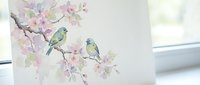 Watercolor painting of two small birds perched on blooming cherry blossom branch with delicate pink flowers against soft background for spring decor.
