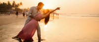 Romantic couple dancing on tropical beach at golden sunset with palm trees and ocean waves creating dreamy vacation atmosphere for wedding or honeymoon.