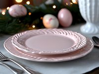 Empty pink ceramic plates with elegant rope pattern trim on festive table setting with Christmas ornaments and pine branches in soft bokeh background.