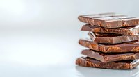 Stack of broken dark chocolate pieces arranged in layers against light background, creating depth and texture for culinary and confectionery designs.