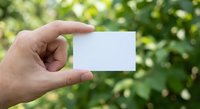 Hand holding blank white business card outdoors with green bokeh background for mockup design and branding presentation purposes.