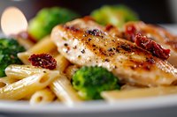 Grilled chicken breast with penne pasta, sun-dried tomatoes and steamed broccoli on white plate, close up view of Mediterranean cuisine dinner.