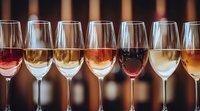 Wine glasses filled with different varieties from white to rose and red arranged in row on bar counter with warm ambient lighting and blurred background.