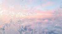 Frost-covered window glass with delicate ice crystals catching soft sunrise light, creating an ethereal winter atmosphere with blurred snowy landscape background.