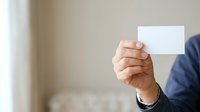 Mature male professional in business attire holding blank white card for custom messaging or branding purposes in corporate setting.