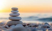 Balanced stones pyramid on beach at sunset with blurred ocean waves background creates peaceful zen atmosphere for wellness and meditation practices.