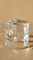 Crystal clear ice cube with water droplets on warm beige surface with dramatic lighting and reflections for beverage and cooling concepts.