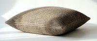 Beige textured throw pillow with waffle knit pattern isolated on white background, perfect for home decor and interior design projects.