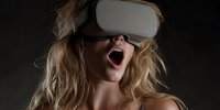 Young blonde woman with open mouth wearing virtual reality headset against dark background, experiencing immersive technology.