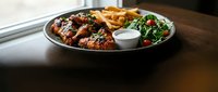 Grilled chicken wings with crispy fries and fresh salad served on dark plate with dipping sauce for restaurant menu and food delivery concepts.