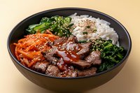 Korean beef bowl with tender sliced meat, steamed rice, sauteed spinach, spicy carrots, sesame seeds and savory sauce served in black ceramic bowl.