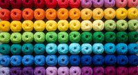 Colorful rainbow gradient yarn skeins arranged in neat rows from red to purple, perfect for crafting, knitting, sewing and textile projects.