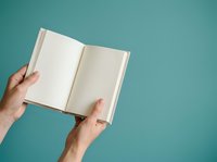 Open book with blank pages held by hands against turquoise background. Suitable for publishing, education, and creative projects.