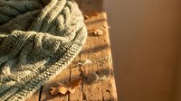 Cozy knitted sweater with cable pattern draped over rustic wooden surface creating warm autumn atmosphere for home decor and lifestyle concepts.