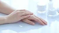 Woman hands applying moisturizer cream with cosmetic jars on white table. Skincare routine and beauty treatment concept for spa and wellness.