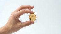 Hand holding a gold coin with tree symbol on light background, representing wealth, investment, and financial growth concept.