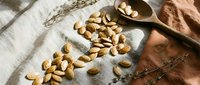 Raw cashew nuts scattered on rustic linen fabric with wooden spoon and dried branches creating natural organic food styling composition for healthy eating.