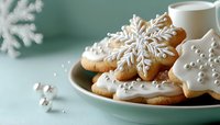 Festive snowflake sugar cookies decorated with white royal icing on mint green background with glass of milk. Holiday baking and winter treats.