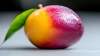 Fresh ripe mango with water drops and green leaf on light background, macro shot showing vibrant yellow and red gradient colors of tropical fruit.