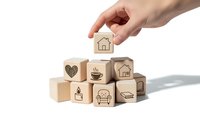 Hand placing wooden cube with house icon on stack of lifestyle blocks isolated on white background for real estate and home concept design.