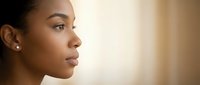 Young African American woman in profile with natural makeup and elegant earrings against soft warm background for beauty and skincare concepts.