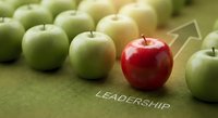 Red apple standing out among green apples with leadership arrow and text on green surface representing uniqueness and business leadership concepts.