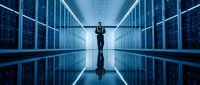 Businessman in formal attire riding bicycle through symmetrical server room with glowing blue data center racks, representing digital innovation and tech infrastructure.