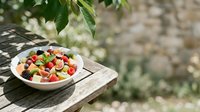 Colorful fruit salad with mixed berries and melon served in white bowl on wooden table outdoors, perfect for healthy eating and summer dining concepts.