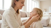 Young Caucasian mother gently touches her toddler child's face, sharing a tender moment of love and care in a bright home interior.