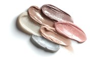 Shimmering cosmetic cream smears in metallic rose gold, silver, and pearl tones on white background, showcasing luxury makeup texture.