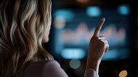 Young blonde woman pointing at financial chart on dark screen with blurred bokeh background, analyzing market data and trading statistics.