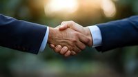 Close-up of business handshake between two professionals in dark suits against blurred natural background with warm sunset bokeh lighting effect.