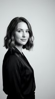 Professional young Caucasian businesswoman with wavy bob haircut in black blazer posing confidently against neutral background for corporate headshot.