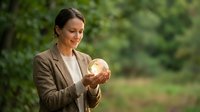 Professional businesswoman in beige suit holding golden piggy bank outdoors, smiling while planning financial savings and investment strategies for future.