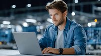 Young professional man working on laptop in modern office environment with focused concentration and contemporary workspace lighting.