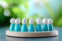 Small blue and white wooden figures arranged in circle on gray platform against blurred green background representing team, unity and collaboration concept.