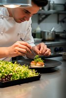 Professional male chef carefully plating gourmet dish with microgreens in modern commercial kitchen. Culinary artistry and fine dining preparation concept.