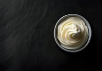 Creamy white mayonnaise sauce swirled in ceramic bowl on dark black stone background, top view with copy space for food photography and menu design.