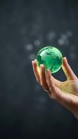Human hands holding glowing green glass globe representing Earth with continents visible against dark bokeh background for environmental protection concepts.