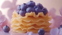 Fresh blueberries on crispy waffle cone with cream, delicious summer dessert for cafe menu, food photography with purple flower petals background.