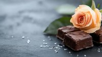 Fresh peach rose with dark chocolate pieces and sea salt crystals on black slate background, romantic food photography for confectionery and dessert menus.