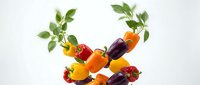 Colorful sweet bell peppers and green leaves arranged in a dynamic circular composition on a white background, fresh organic vegetables.