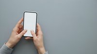 Hands holding smartphone with blank white screen against gray background for app mockup and digital marketing.