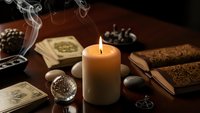 Mystical fortune telling setup with burning candle, tarot cards, crystal ball and ancient scrolls creating atmospheric divination scene for spiritual practices.