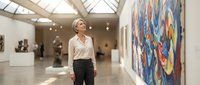 Young African American woman admiring colorful abstract artwork in modern art gallery with natural lighting from glass ceiling.