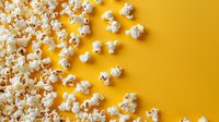 Fresh popcorn scattered on vibrant yellow background, perfect for food blog, cinema promotion, or snack advertising. Creative flat lay composition with copy space.