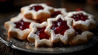 Star-shaped shortbread cookies with red jam filling and powdered sugar dusting on vintage plate, homemade holiday baking for festive celebrations.