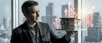 Mature male professional in business suit holding miniature house with rising percentage symbols and upward arrow, representing real estate investment growth and property value appreciation against urban skyline.