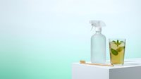 Spray bottle with fresh mint beverage on geometric platform against turquoise gradient background, suitable for cleaning product, wellness, and beverage marketing campaigns.
