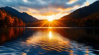 Stunning autumn sunrise over mountain lake with golden sunburst and vibrant fall foliage reflected in calm water creating peaceful morning landscape scene.